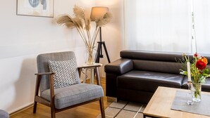 Un salon moderne avec un fauteuil gris, un canapé en cuir noir, une lampe sur pied et un vase de fleurs posé sur une table.