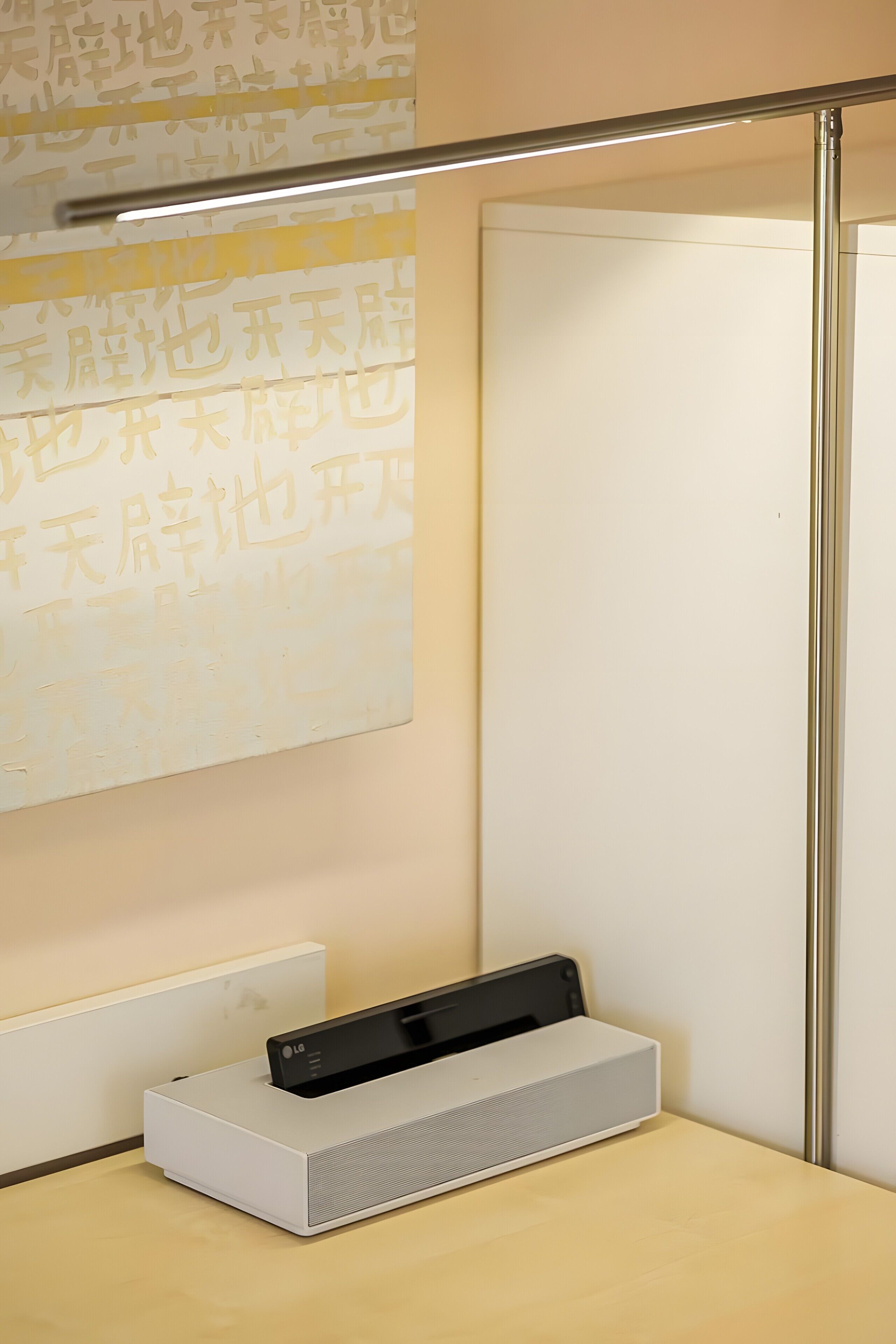 Ein Zimmer mit weißer Wand, einem gerahmten Kunstwerk, einem weißen Tisch und einem weißen Lautsprecher.