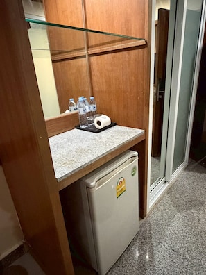 A compact kitchenette with a small refrigerator, a countertop, and a glass shelf holding water bottles and a roll of paper towels. - Palette Jomtien Beach Pattaya (Pattaya)