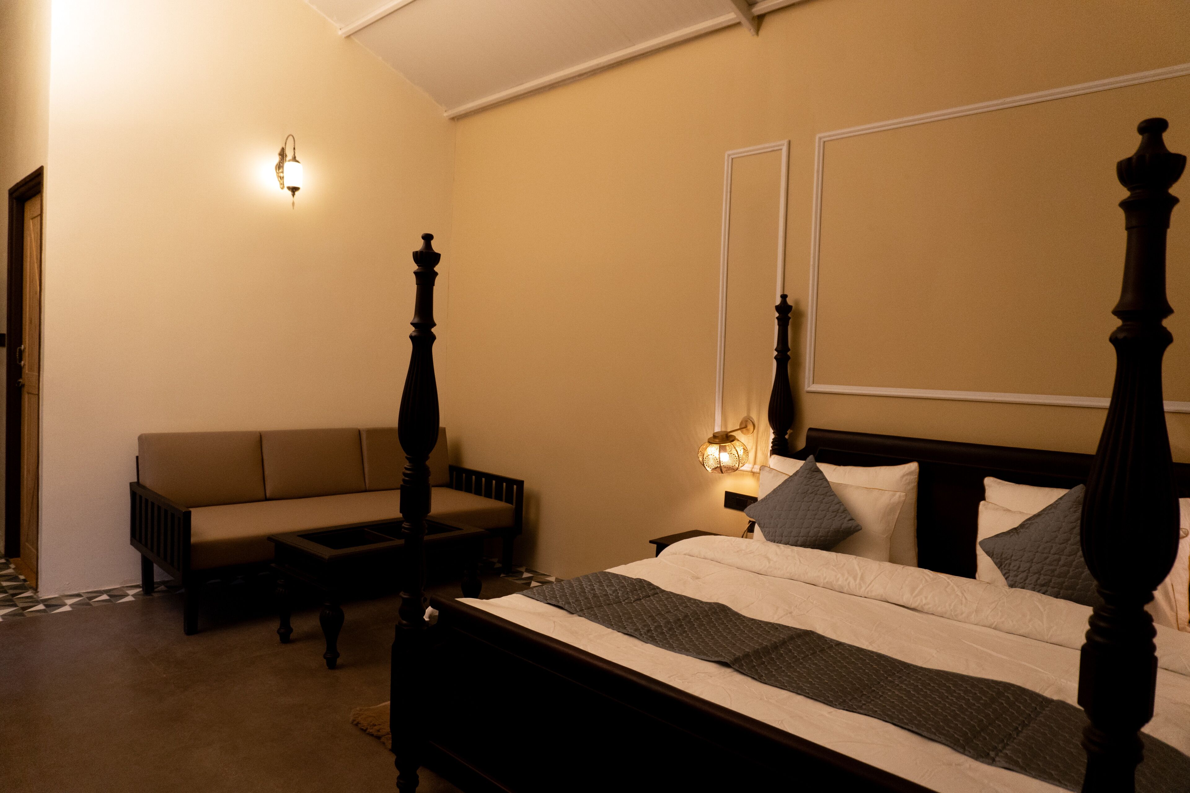 Quarto com cama de dossel, sofá e duas luminárias fixadas na parede.