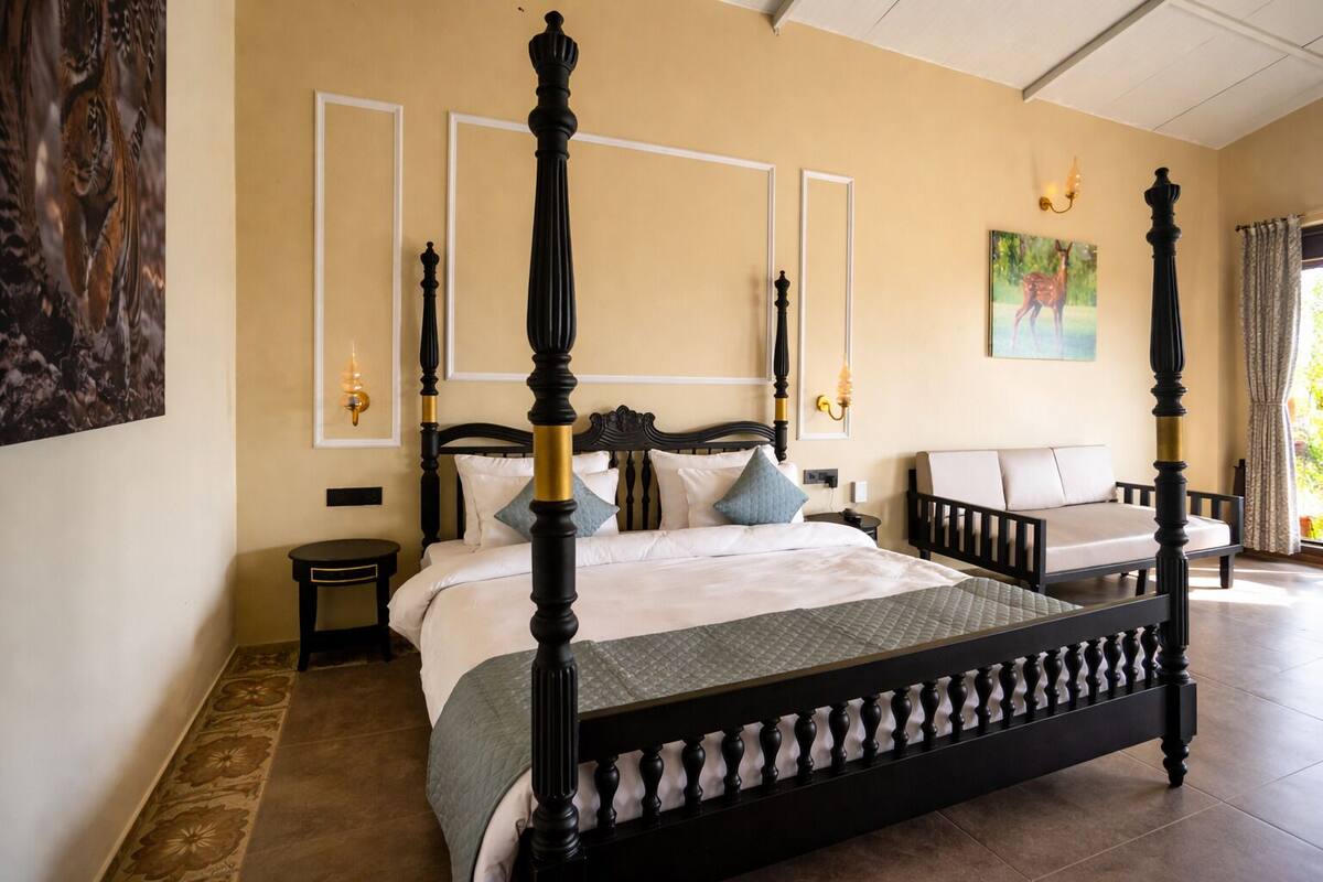 Un lit à baldaquin avec une structure sombre et des détails dorés, un canapé avec un coussin de couleur claire, et un tableau représentant un cerf accroché au mur.