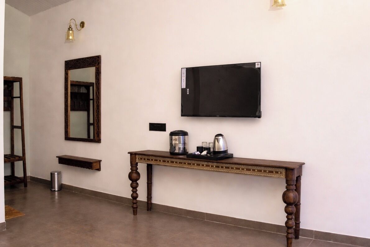 A hotel room with a wooden console table, a flat-screen TV, a mirror, and a small shelf.