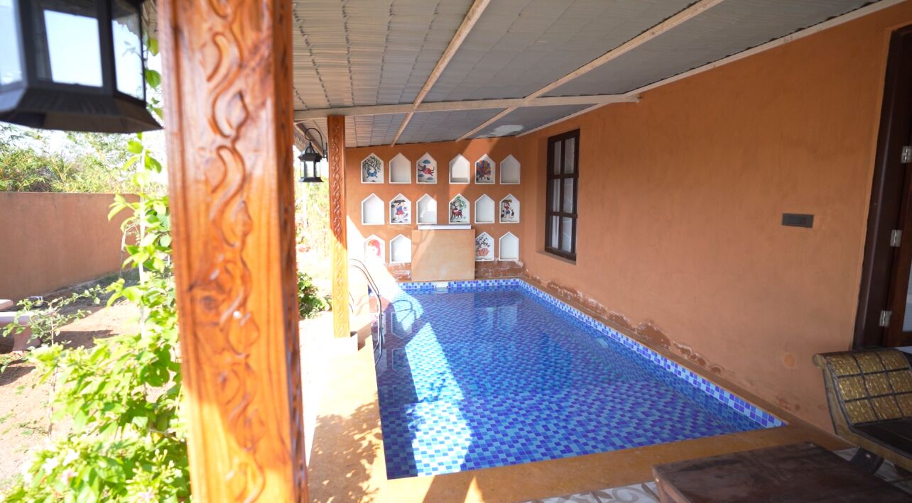 Una piccola piscina con piastrelle blu, una panca di legno e un muro con finestre decorative.