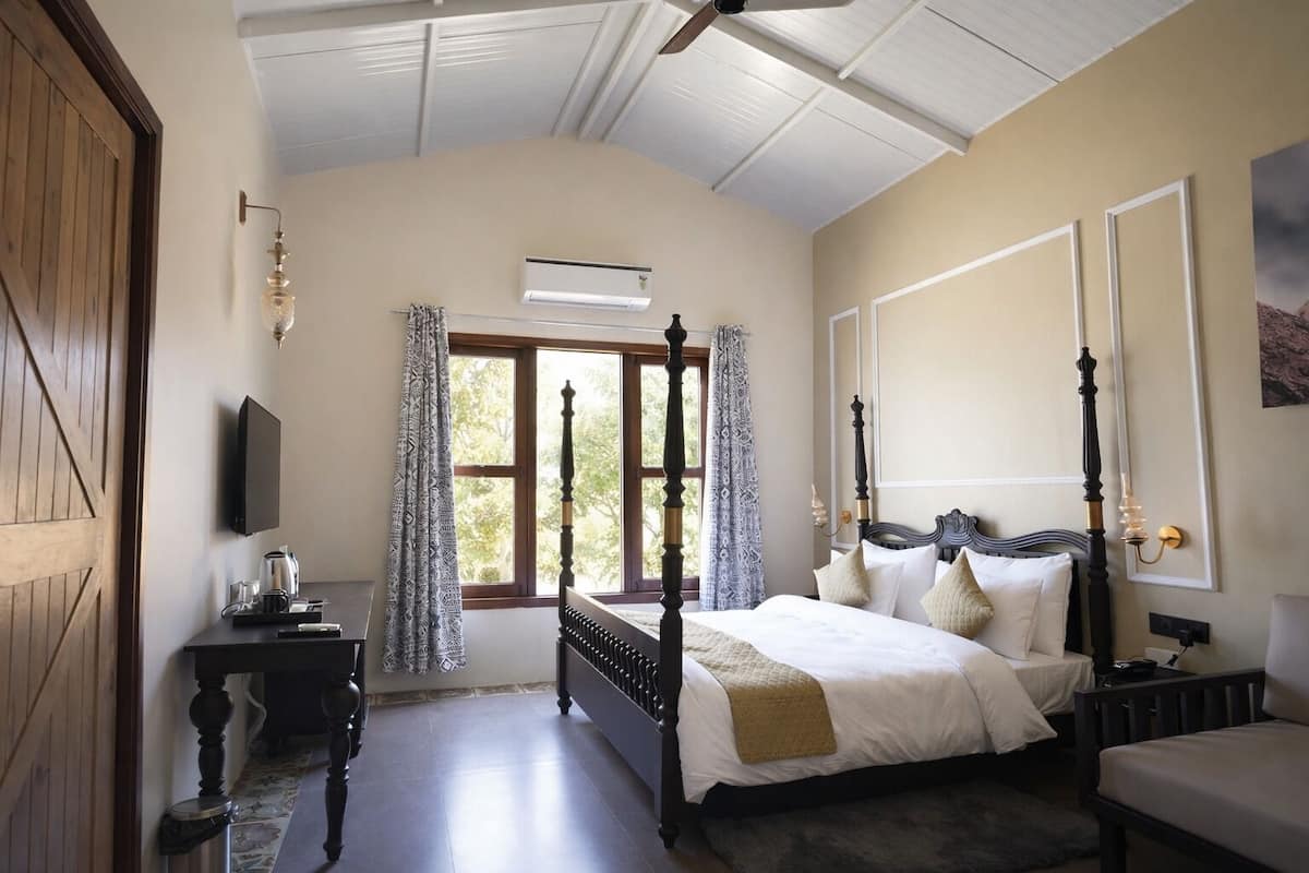 Une chambre à coucher avec un lit à baldaquin, une table de chevet, un téléviseur fixé au mur et une fenêtre avec des rideaux.