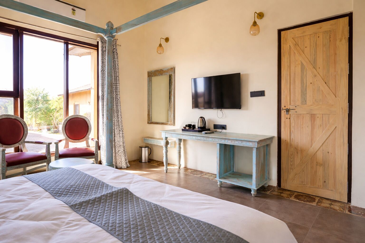 Quarto com cama, escrivaninha, televisão e uma grande porta de madeira.