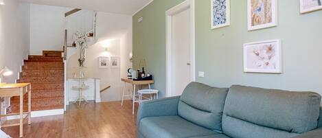 A living room with a grey sofa, wooden flooring, a staircase, and a small table with a lamp.