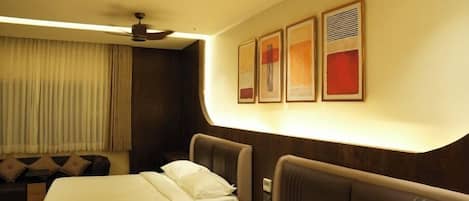 A hotel room with two beds, a ceiling fan, a sofa, and artwork on the wall.