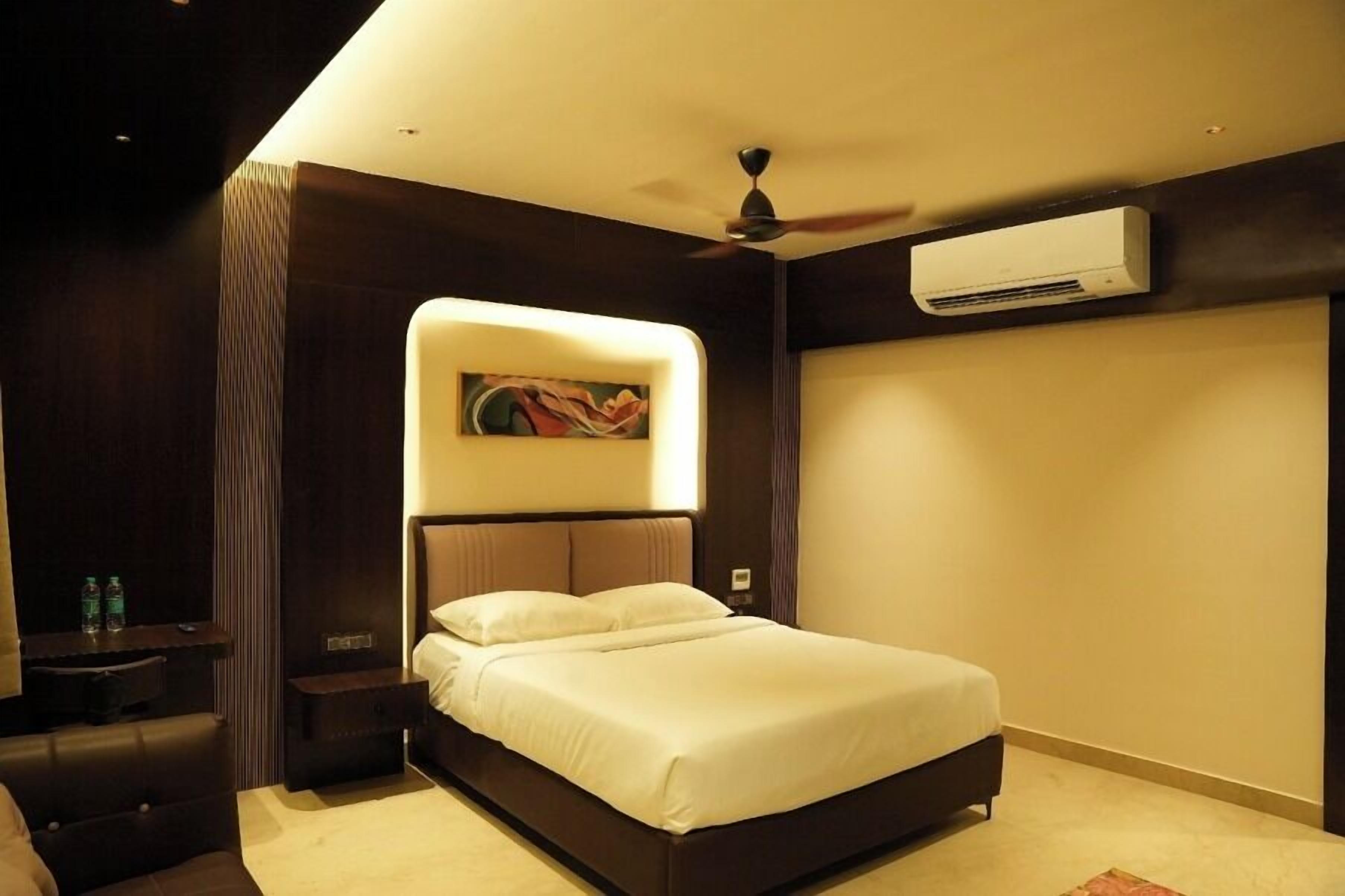 Una habitación de hotel moderna con una cama grande, un ventilador de techo, un equipo de aire acondicionado y un cuadro sobre la cama.