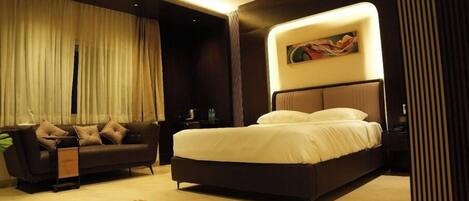 A bedroom with a bed, a sofa, a ceiling fan, and a painting on the wall.