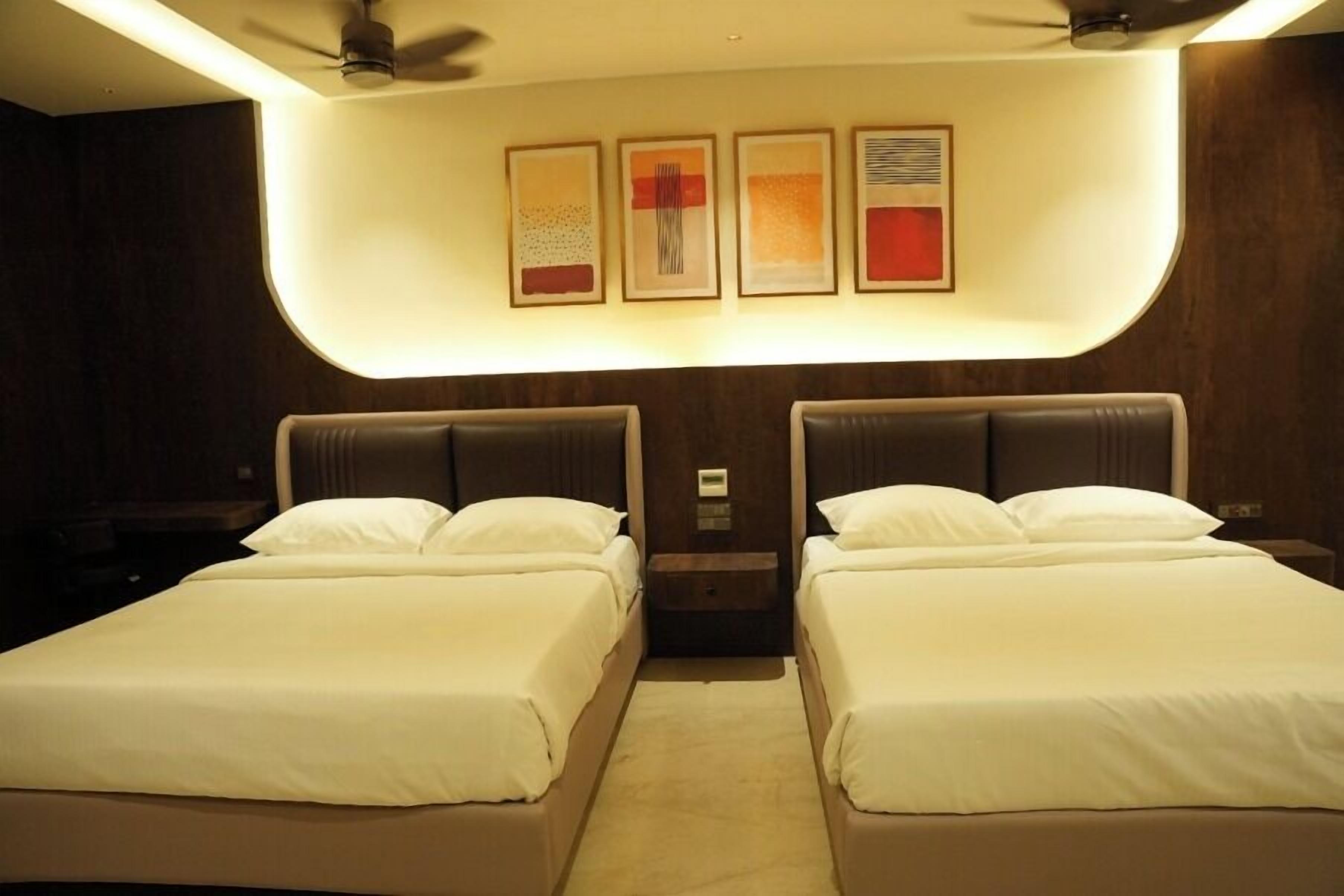 A hotel room with two beds, a ceiling fan, and wall-mounted artwork.