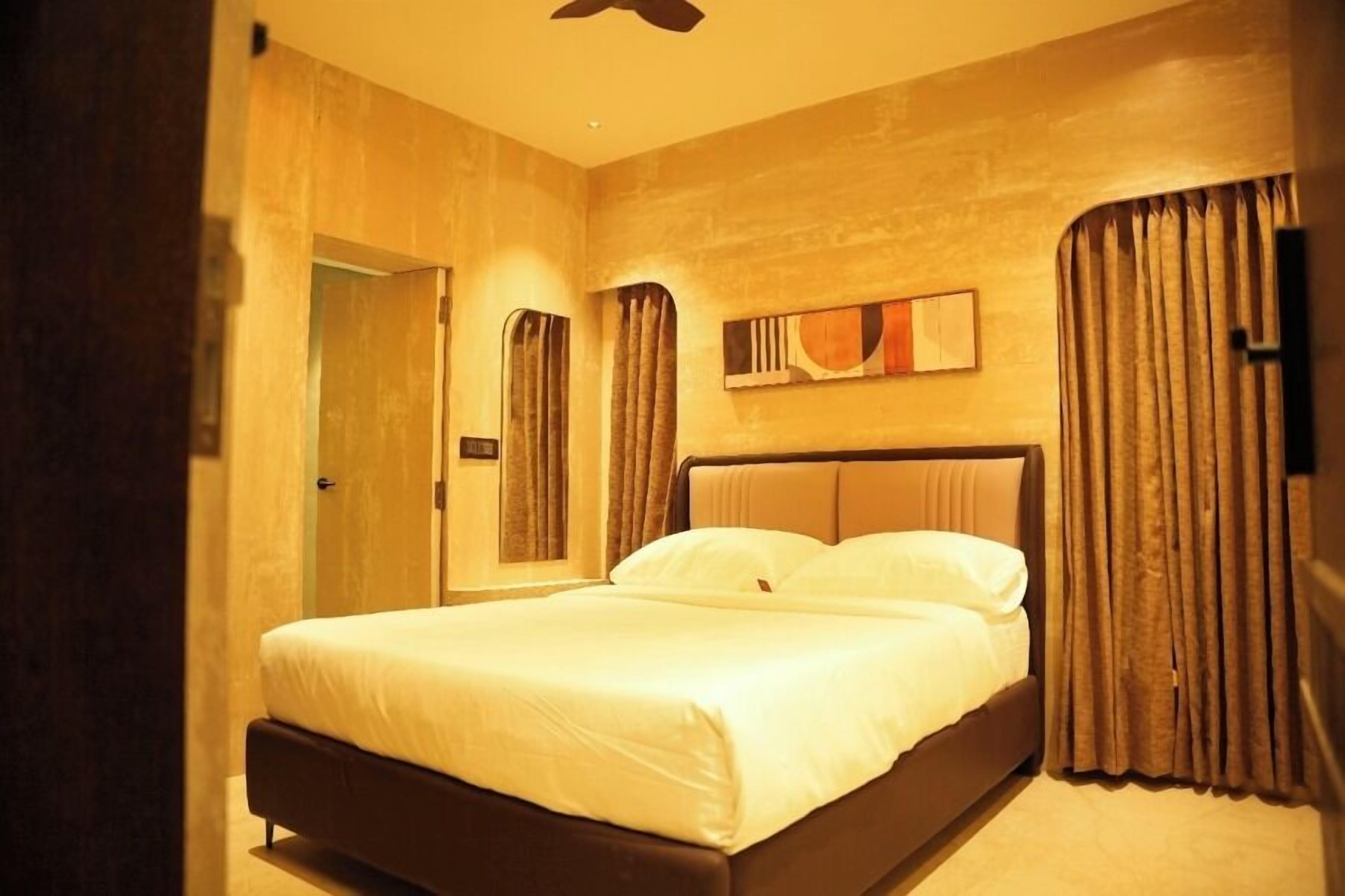 A hotel room with a bed, curtains, a painting on the wall, and a door.