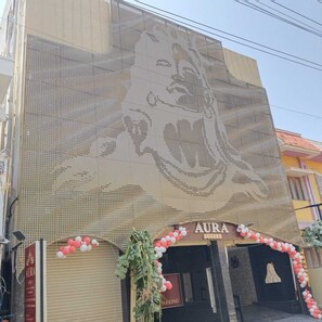 A building facade with a large, intricate wall art depicting a figure. The entrance has a sign reading 'AURA SUITES' and is decorated with balloons. - Aura Suites (Tiruvannamalai)