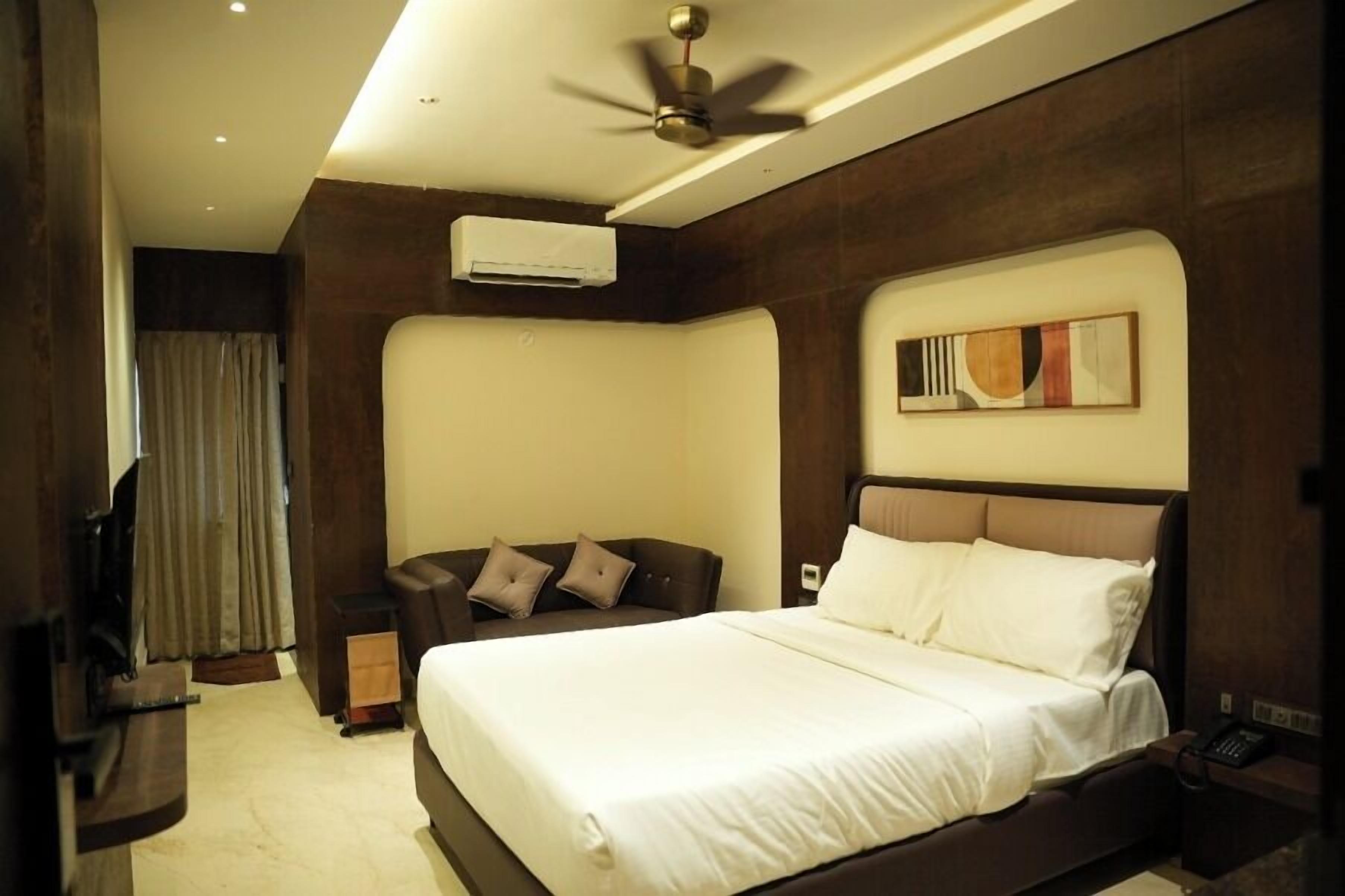 Una habitación de hotel con cama, sofá, aire acondicionado, ventilador de techo y un cuadro en la pared.