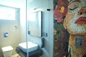 A bathroom with a white sink, a mirror, and a mosaic wall. - Aura Suites (Tiruvannamalai)