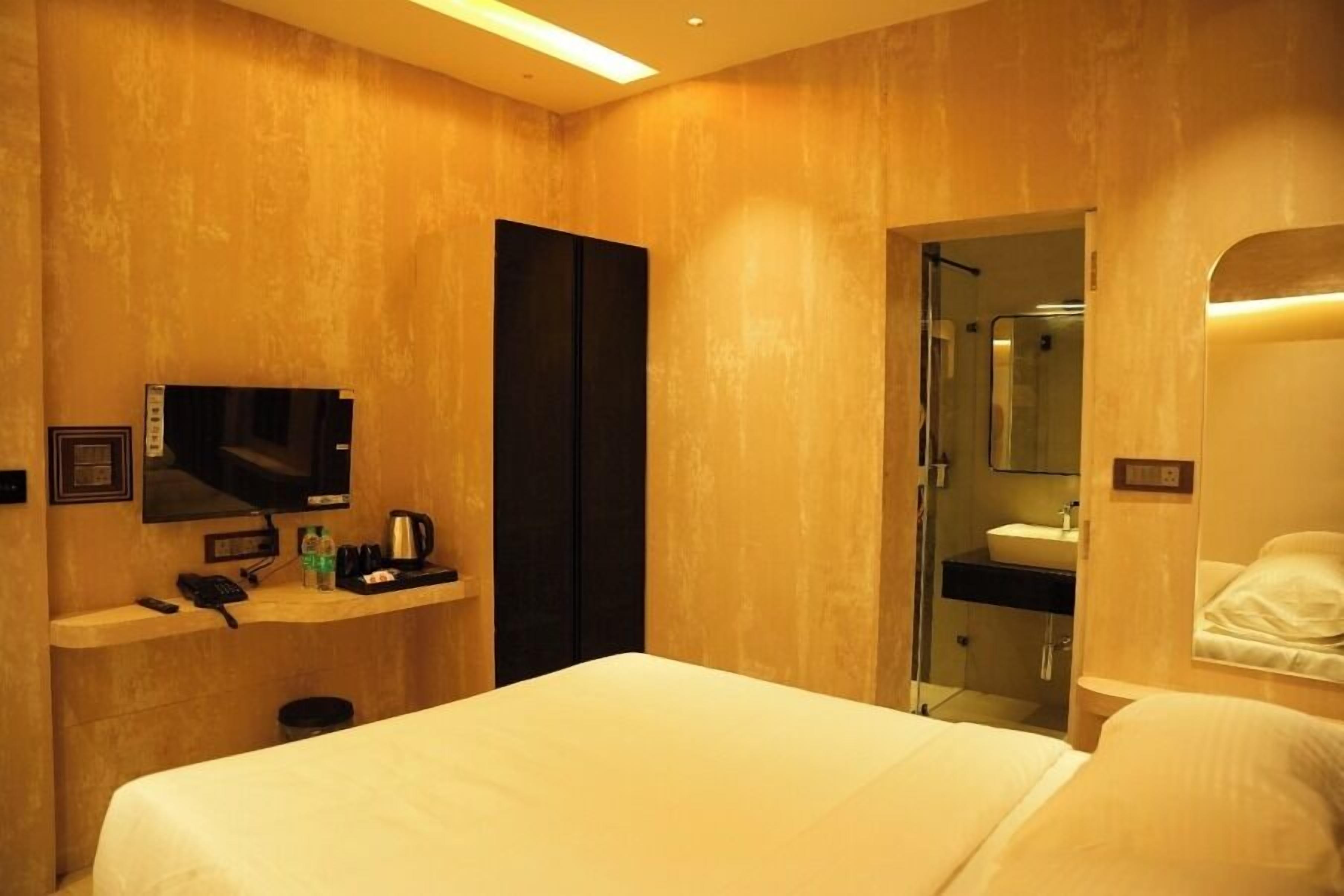 Une chambre d’hôtel équipée d’un lit, d’une télévision, d’un bureau avec un téléphone et une machine à café, d’un miroir et d’une salle de bain visible à travers une porte ouverte.