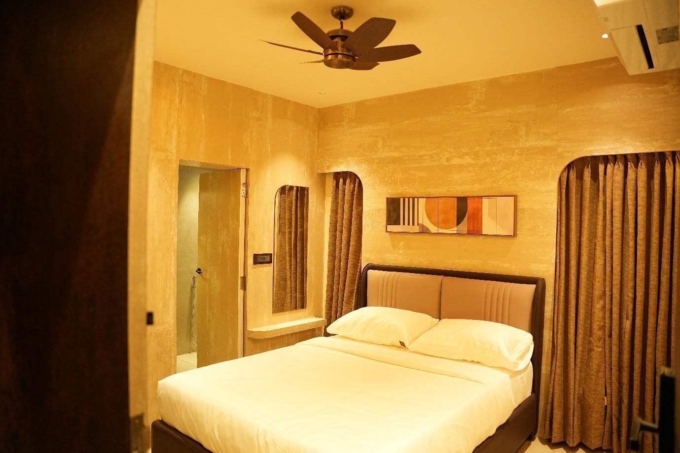 Une chambre d’hôtel avec un lit, un ventilateur de plafond, une fenêtre avec des rideaux et une œuvre d’art accrochée au mur.