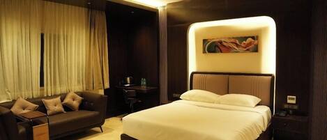 A modern hotel room with a large bed, a sofa, a desk, and a ceiling fan.