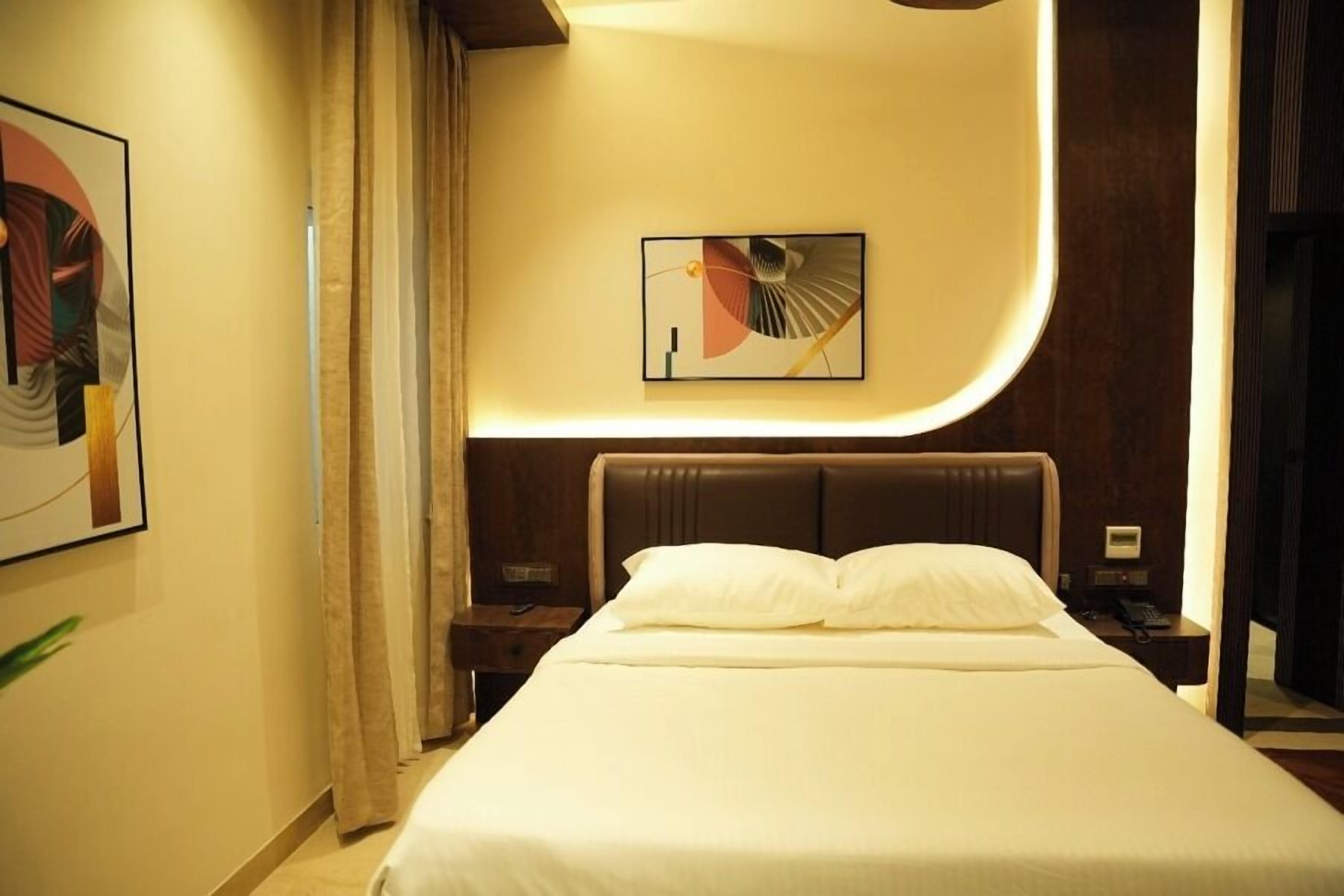 Una habitación de hotel con cama, mesita de noche, una obra de arte en la pared y una puerta.