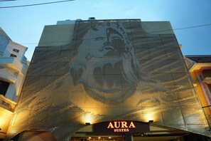 A building with a large, illuminated wall art installation and the sign 'AURA SUITES' below it. - Aura Suites (Tiruvannamalai)