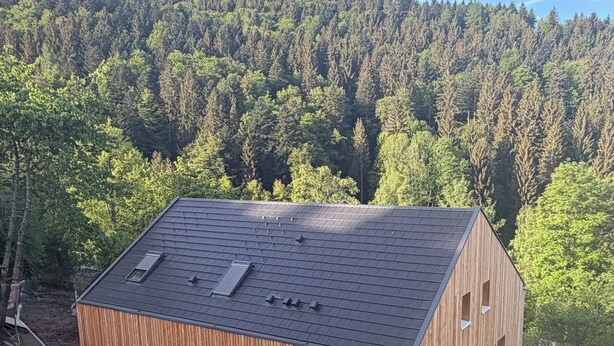 Ein modernes Holzgebäude mit geneigtem Dach, umgeben von einem bewaldeten Gebiet.