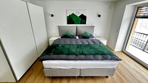 Ein modernes Schlafzimmer mit einem Bett, Nachttischen, einem Fenster und einem an der Wand hängenden Kunstwerk.