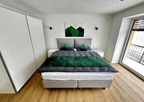 Ein modernes Schlafzimmer mit einem Bett, Nachttischen, einem Fenster und einem an der Wand hängenden Kunstwerk.