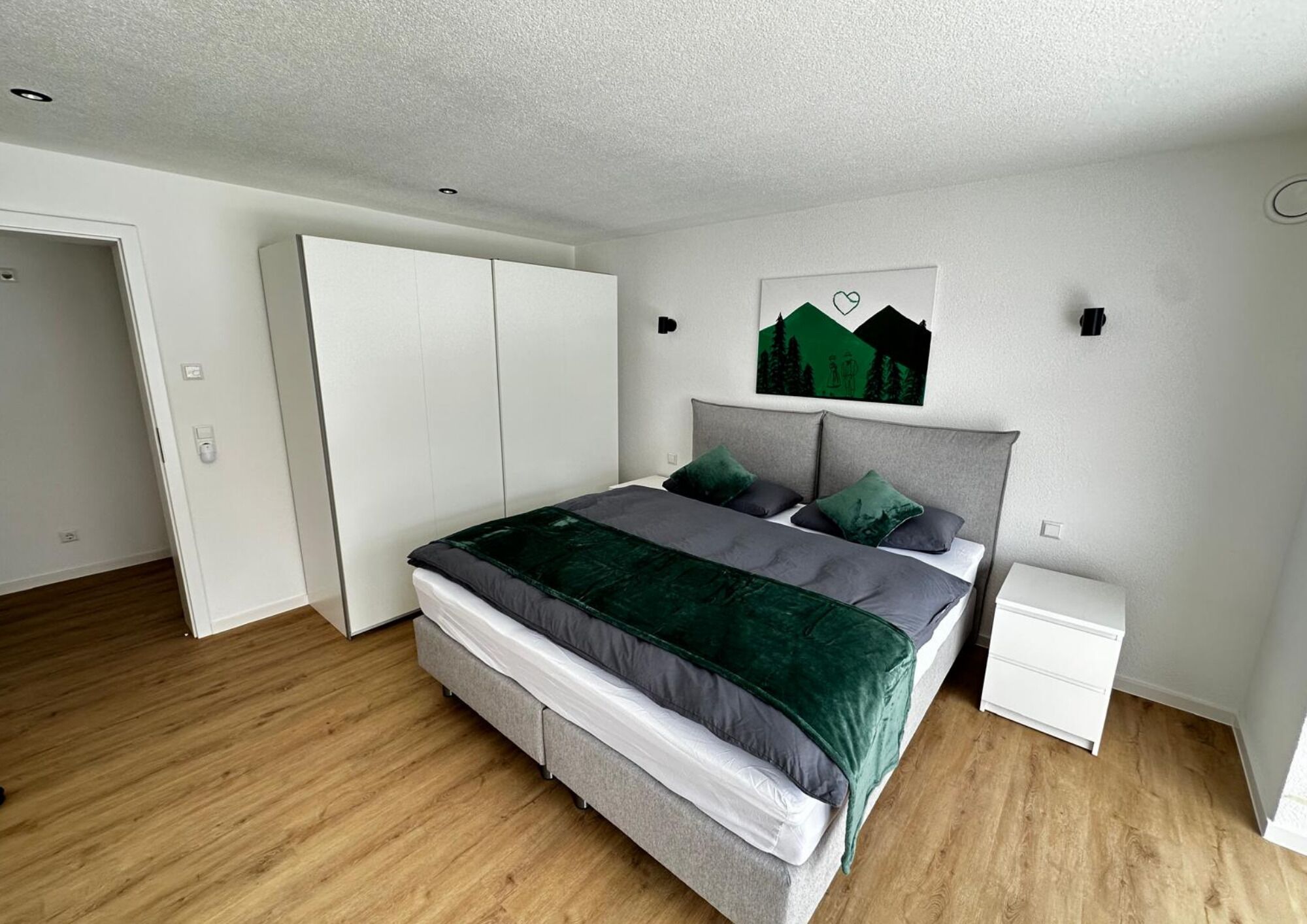 Une chambre à coucher comprenant un lit, une table de chevet, une armoire et une œuvre d’art accrochée au mur.