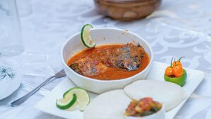 A bowl of fish stew with lime garnish, a plate of flatbreads, and a small green chili pepper. - Nalipiri eco resort  (Mulanje)