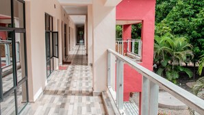 A corridor with a checkered floor, glass doors, and a red building section with a railing. - Nalipiri eco resort  (Mulanje)