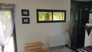 Un dormitorio con cama, ventana con vista a palmeras, radiador y banca de madera.
