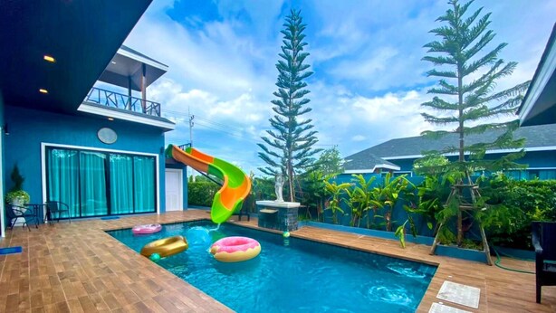 Ein Swimmingpool mit Rutsche, umgeben von tropischen Pflanzen und einer Holzterrasse.