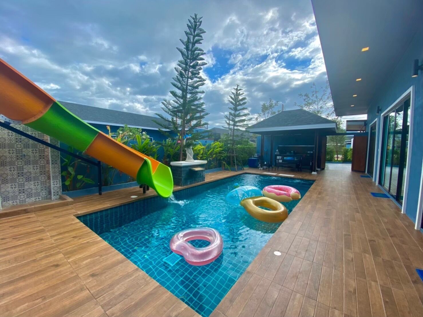 A swimming pool with a slide, inflatable rings, and a covered seating area.