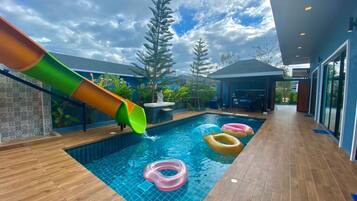 A swimming pool with a slide, inflatable rings, and a covered seating area.