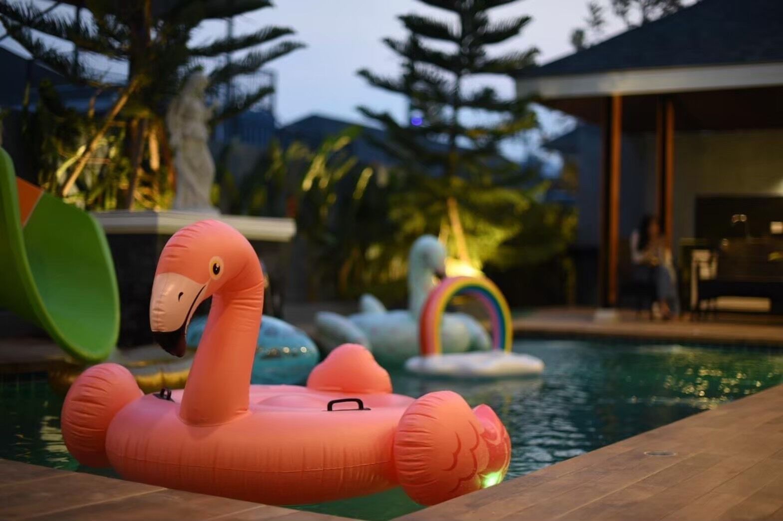 A swimming pool with inflatable flamingo and rainbow floatation devices.