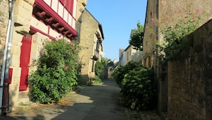 A narrow street with stone buildings, a red door, and lush greenery. - LA PETITE MAISON DE KERTHOMAS - CLASS 3* GÎTE (plumergat)