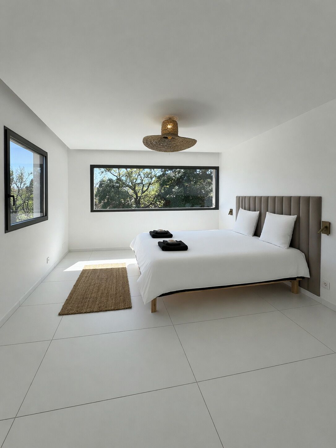 Una camera da letto moderna con un letto grande, una finestra vista alberi, una lampada a soffitto in rattan e un piccolo tappeto.