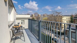 A balcony with a table and chairs, overlooking a cityscape with buildings and a clear sky.