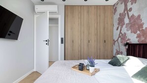 A bedroom with a bed, a bedside table with a tray, a potted plant, and a television mounted on the wall.