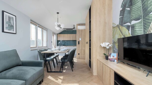 A modern living space with a sofa, dining table, chairs, a TV, and a kitchen area.