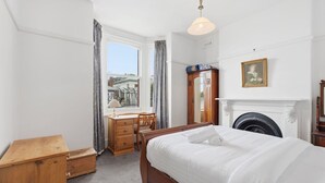 Ein Schlafzimmer mit Bett, Schreibtisch, Stuhl, Kleiderschrank, Kamin und einem Fenster mit Vorhängen.