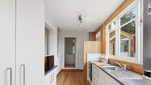 Eine schmale Küche mit weißen Schränken, einer Holzarbeitsplatte, einem Spülbecken und einem Fenster.
