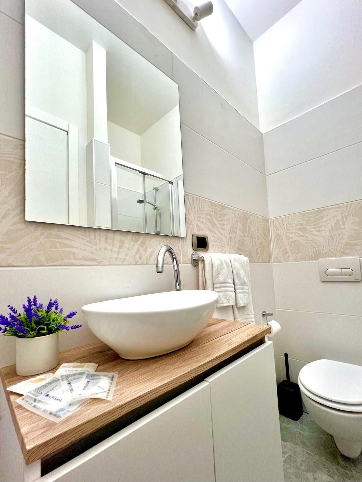 A modern bathroom with a large mirror, a vessel sink, a toilet, and a small potted plant.