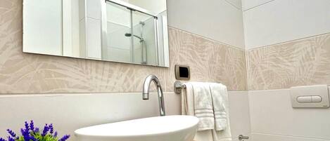 Un baño moderno con un espejo grande, un lavabo sobre encimera, un inodoro y una pequeña planta en maceta.