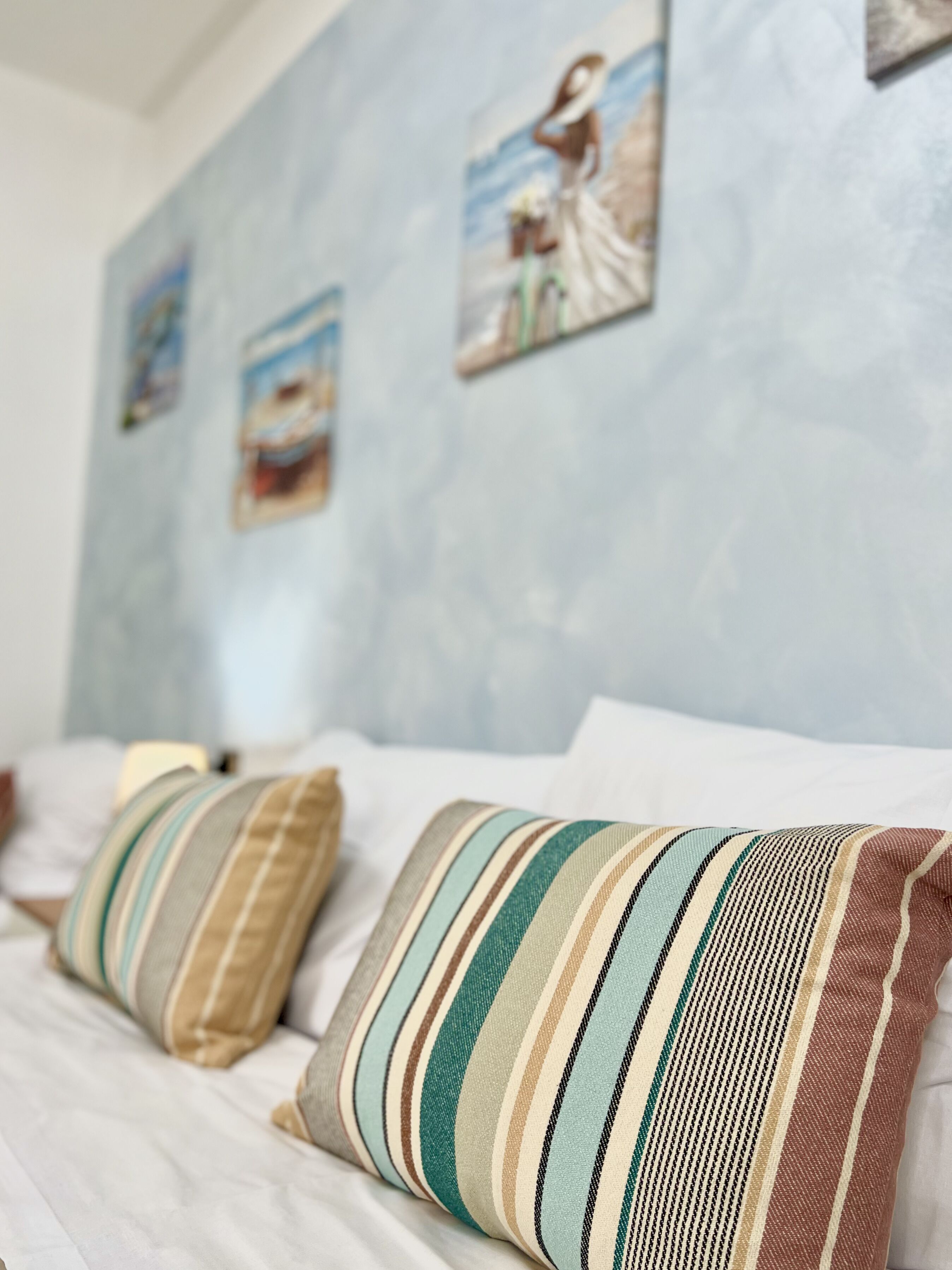 Un lit avec des coussins à rayures et un mur orné de tableaux encadrés.