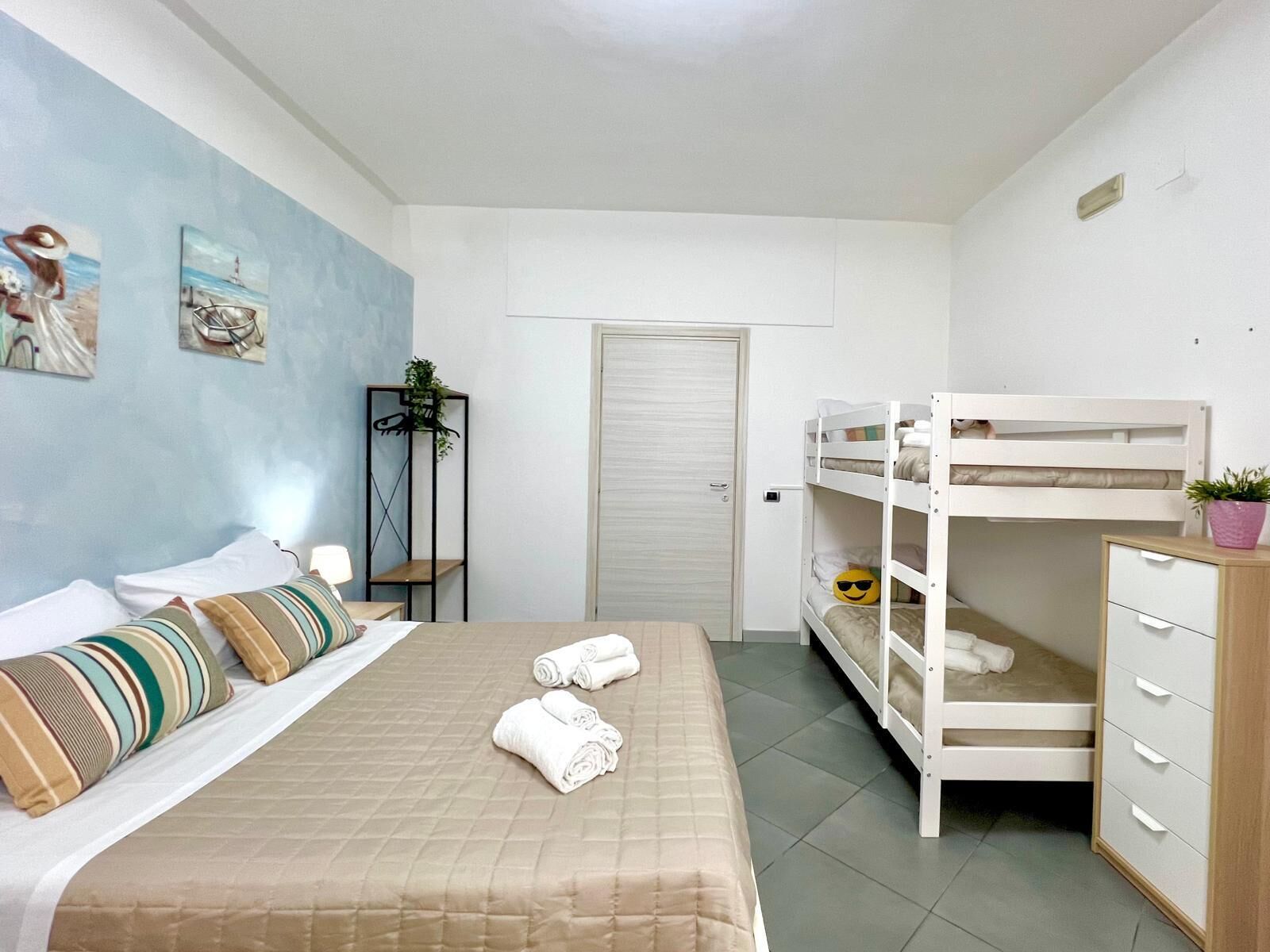 A bedroom with a bed, bunk beds, a wardrobe, a door, and wall art.