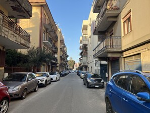 A narrow urban street lined with multi-story residential buildings, parked cars, and balconies with railings. - Elios Rooms Tro (Tropea)