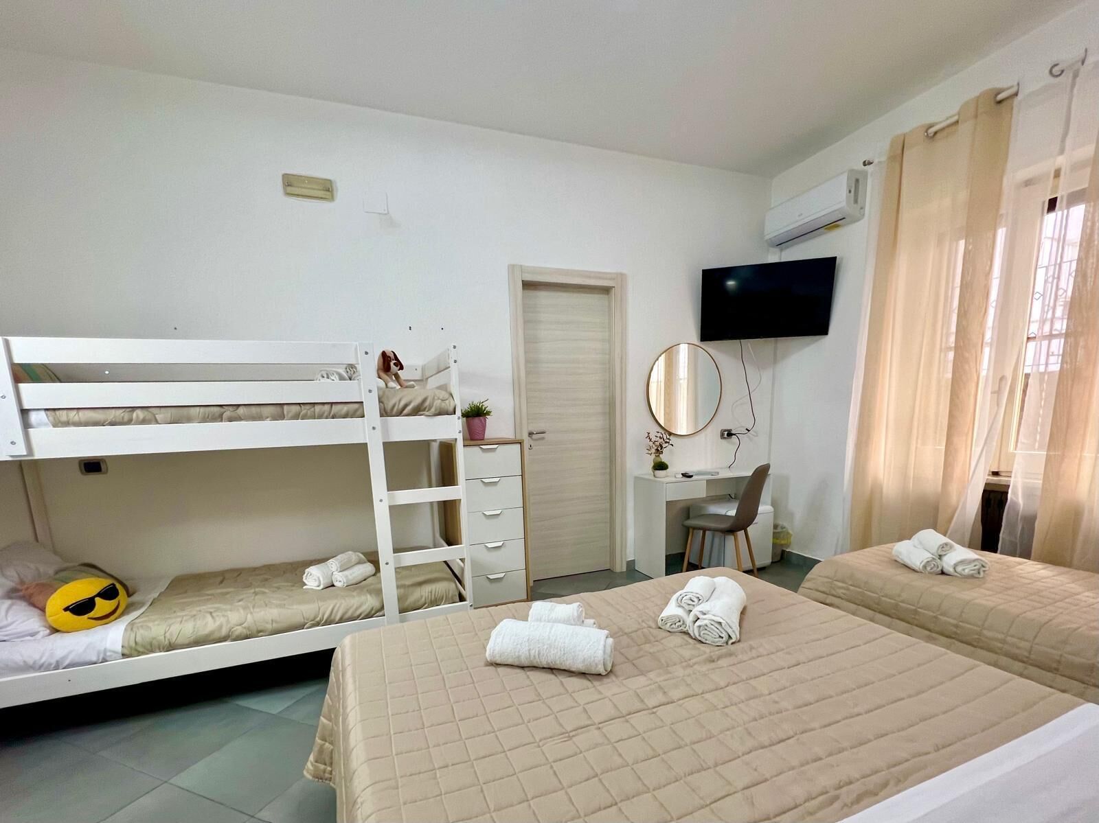 A hotel room with bunk beds, a desk with a chair, a TV, and a window with curtains.