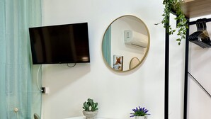 A room with a desk, chair, TV, mirror, air conditioner, potted plants, and a shelf. - Elios Rooms Tro (Tropea)