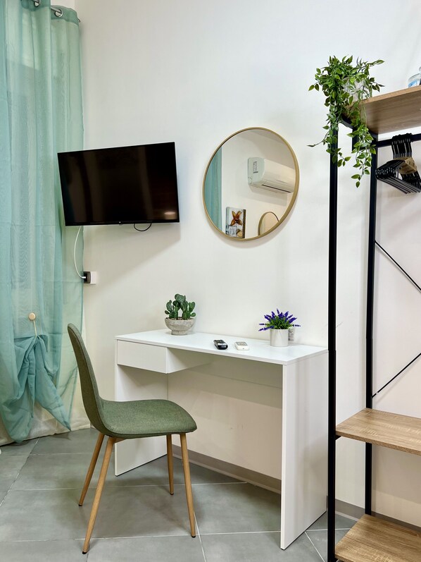 A room with a desk, chair, TV, mirror, air conditioner, potted plants, and a shelf. - Elios Rooms Tro (Tropea)