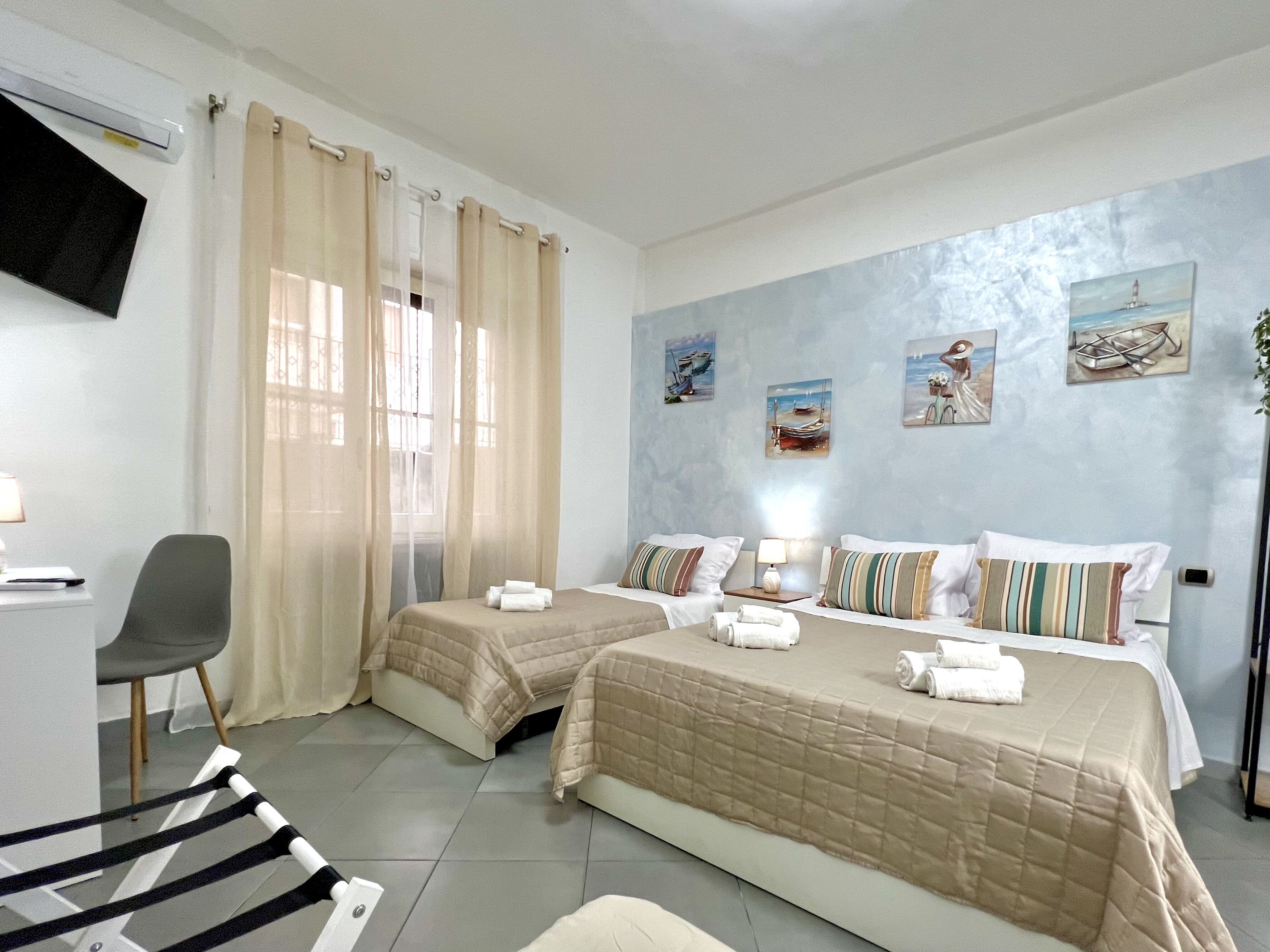 Quarto de hotel com duas camas, uma escrivaninha, uma cadeira e uma televisão na parede.